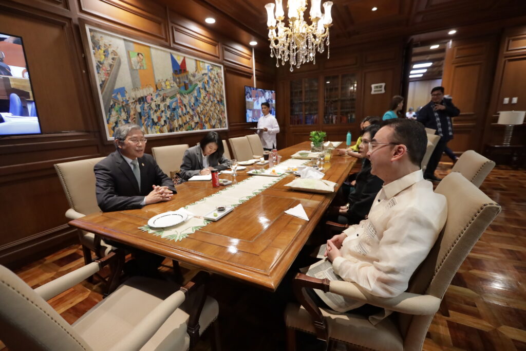 Alan Peter Cayetano attends a formal meeting, possibly discussing policy or governance, in a wood-paneled room with colleagues.