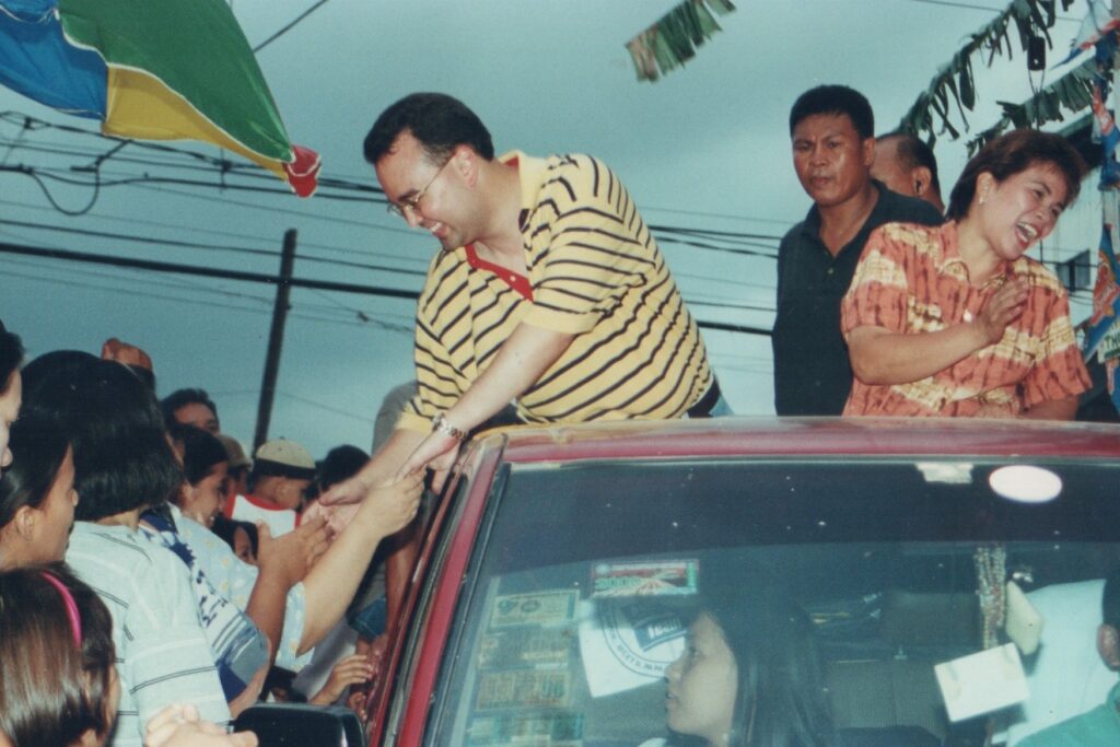 Alan Peter Cayetano greets supporters from a car, shaking hands, engaging during a campaign, showing approachability and connection